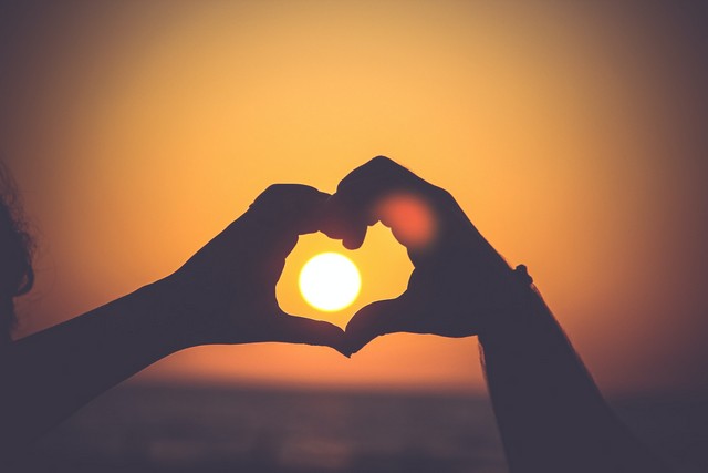 pareja dibujando un corazon con sus manos en el atardecer