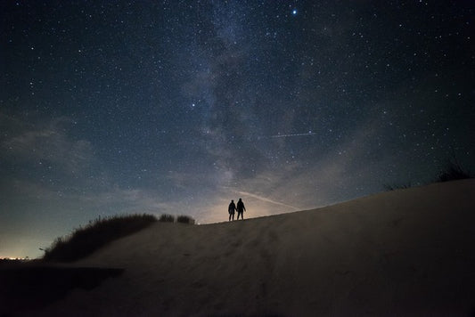 pareja a la lejania tomada de la mano observando el cielo estrellado y con tonos de atardecer