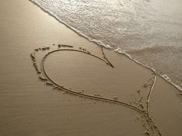 corazón dibujado en la arena siendo borrado en la orilla con el mar