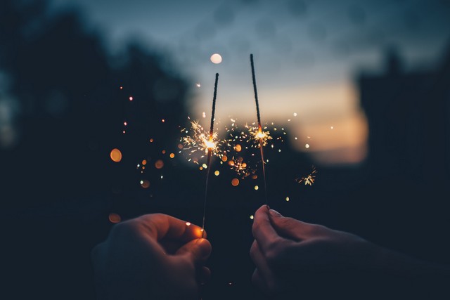 pareja acercando fuego artifical pequeño en sus manos con fondo de la ciudad