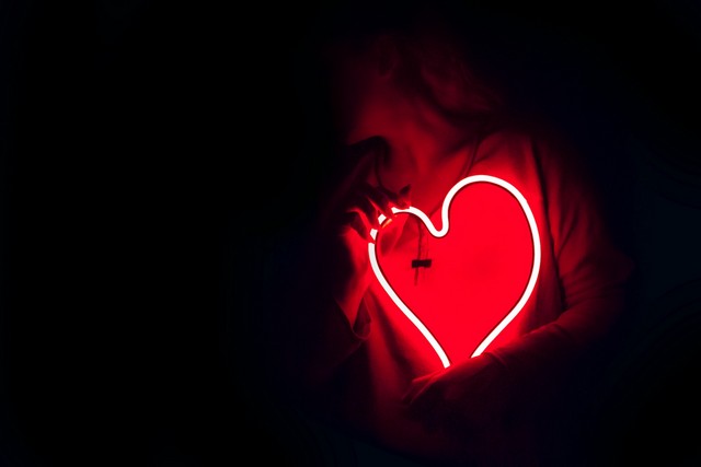 persona sosteniendo un corazon de luz de neón en su pecho en la oscuridad