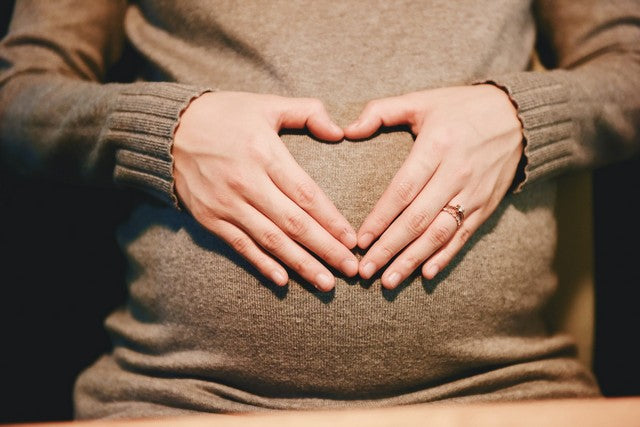 mujer embarazad dibujando un corazón con sus manos sobre su barriga