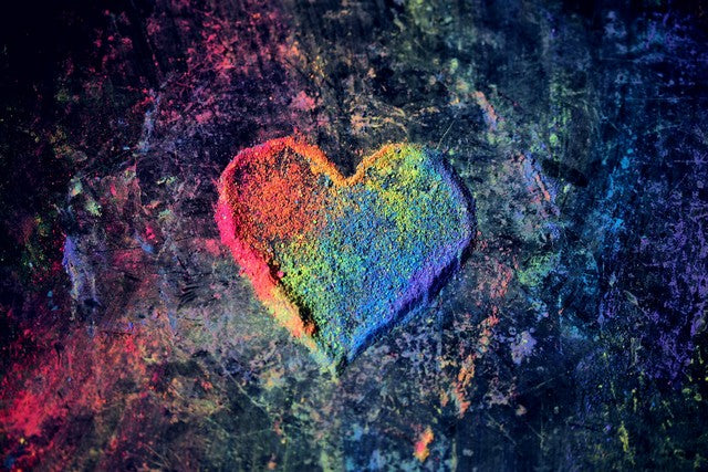 corazón de colores hecho con polvos de colores del arco iris en un fondo azul oscuro