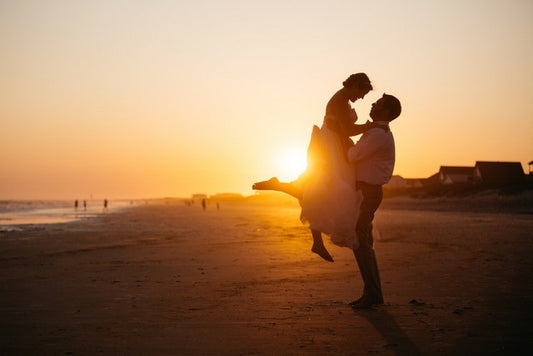  hombre alza a mujer en sus brazos en la playa durante el atardecer
